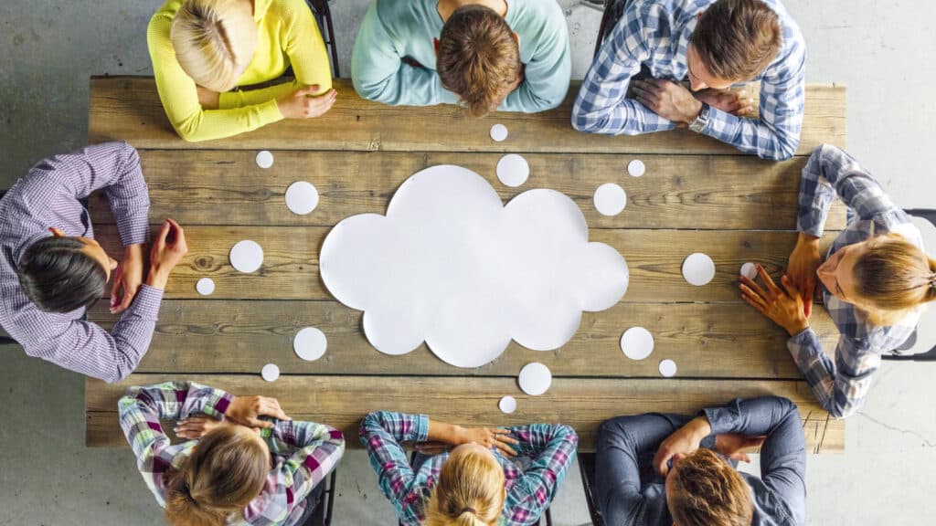 Mehrere Personen sitzen um einen Tisch und sammeln Ideen auf einer Wort-Wolke.
